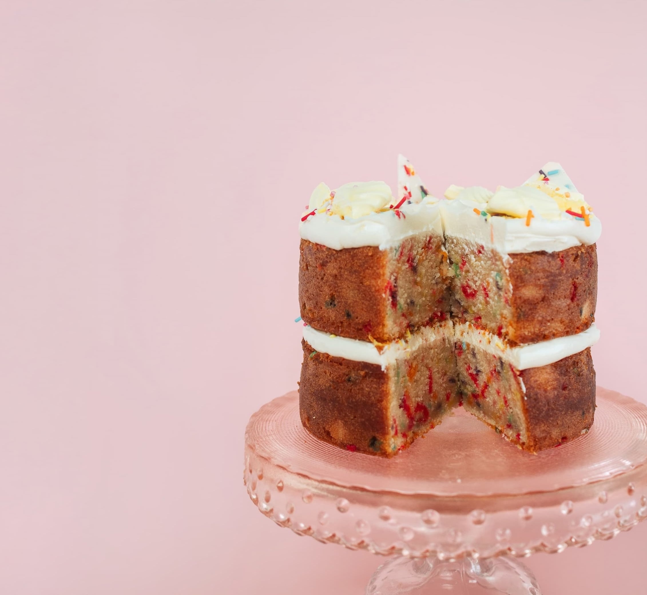 Vanilla sprinkle confetti cake cut open on a cake stand