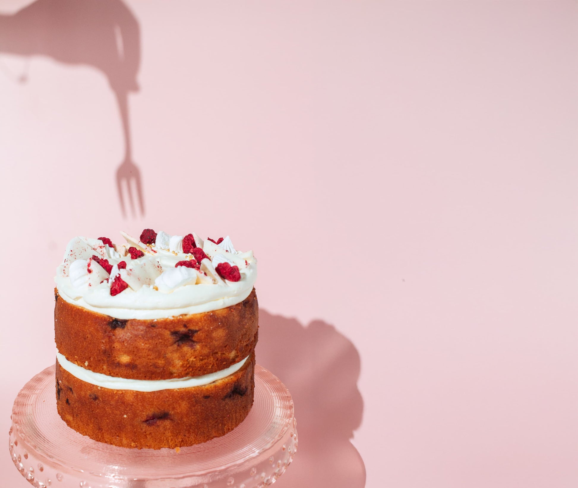 a shadow of a fork going into a lemon raspberry cake