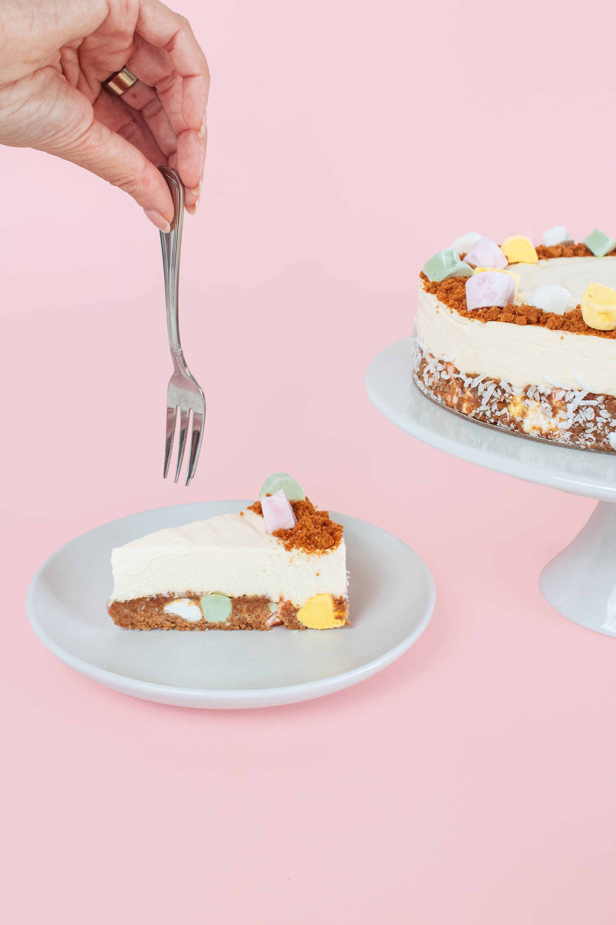 Someone holding a fork above a slice of Lollycake White Chocolate Cheesecake
